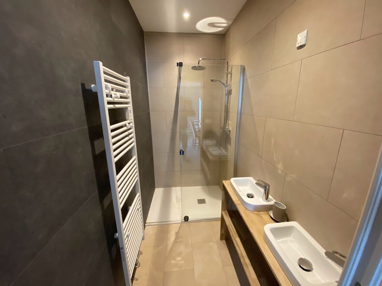 A modern bathroom with a glass-enclosed shower, a white sink, and a towel rack.