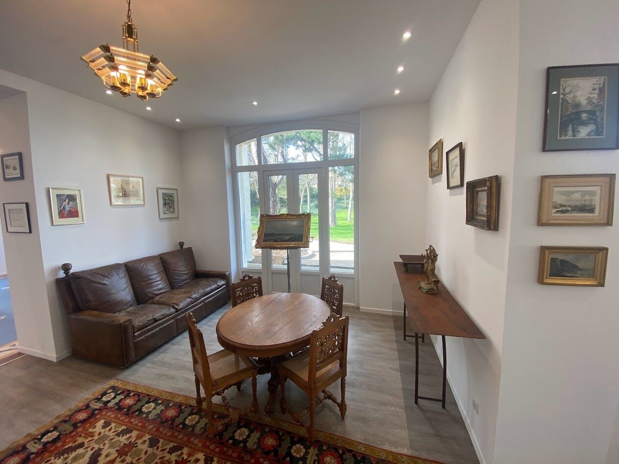 A modern living room with a brown leather sofa, a wooden dining table with chairs, and a chandelier.