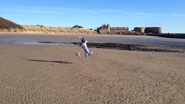 Une plage de sable avec des empreintes et un enfant qui joue au ballon.