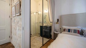 A hotel room with a bed, a bathroom with a shower, a mirror, and a small table. - Authentic Restored Apt In The Old City (Tel Aviv-Yafo)