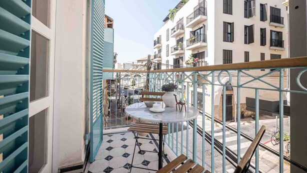 A balcony with a tiled floor, a round table with a potted plant, and wooden chairs. - Authentic Restored Apt In The Old City (Tel Aviv-Yafo)
