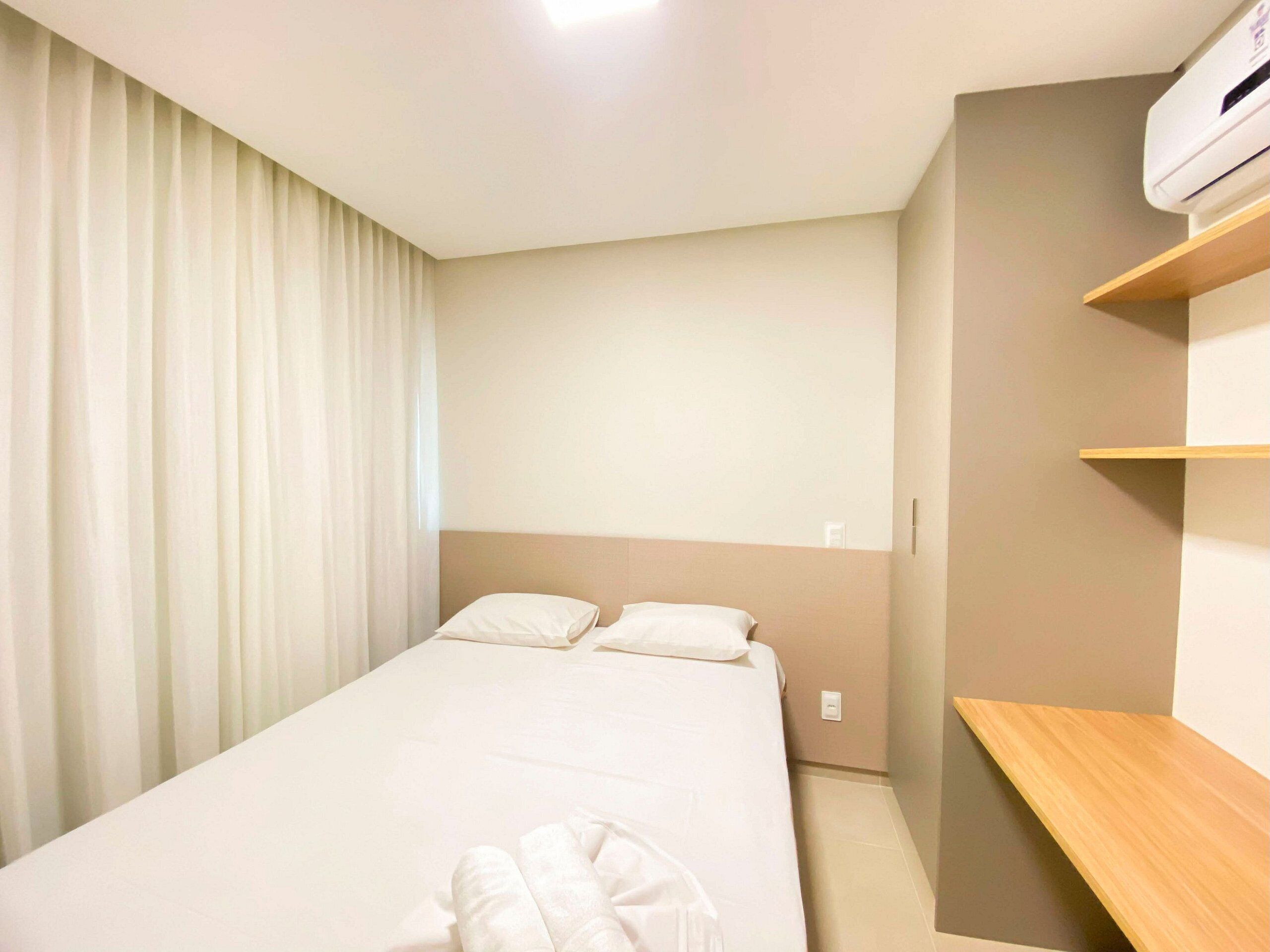 A hotel room with a bed, a wooden shelf, and an air conditioning unit.