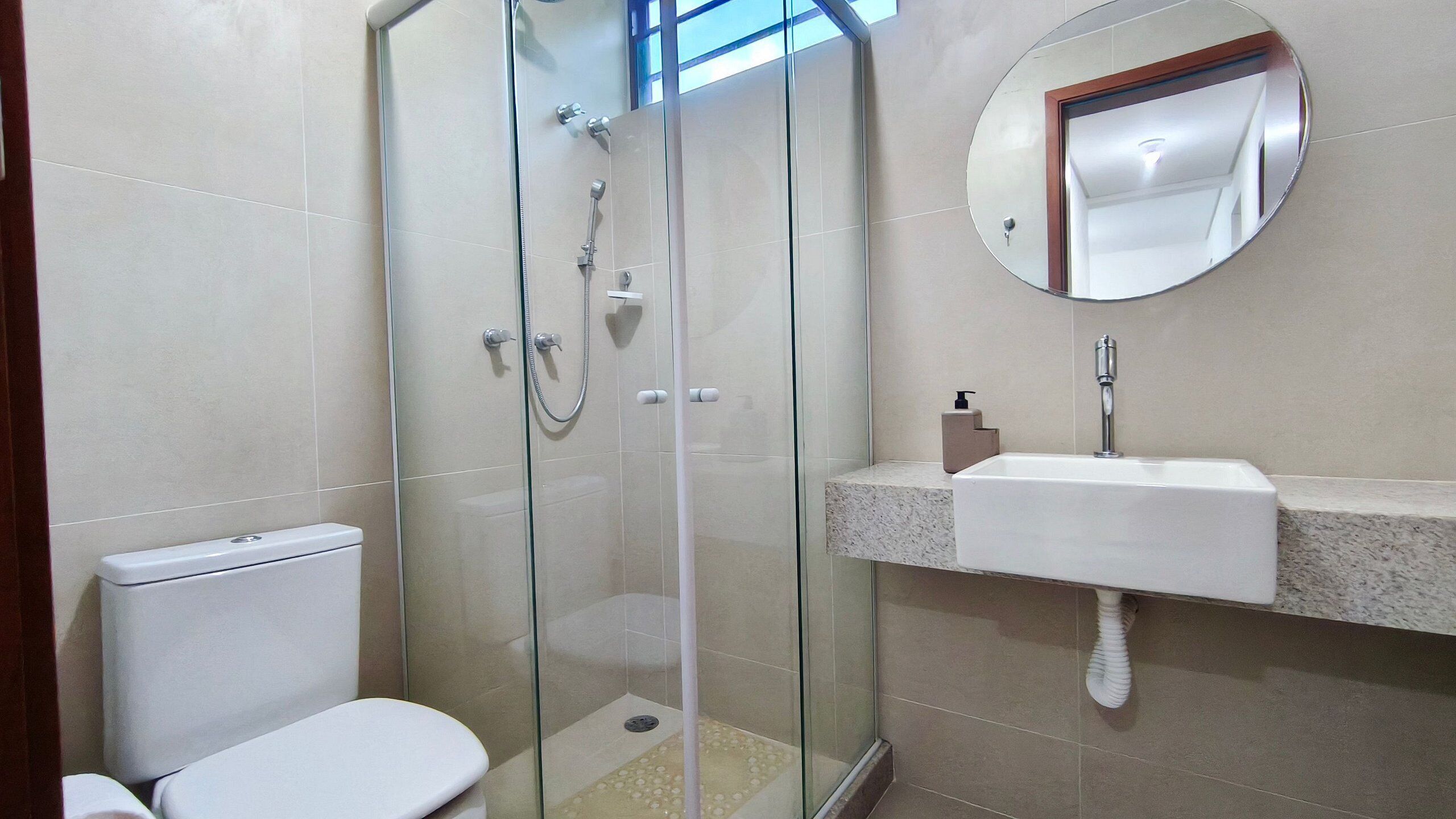 Ein Badezimmer mit Duschkabine, Toilette, Waschbecken mit Spiegel und Seifenspender.