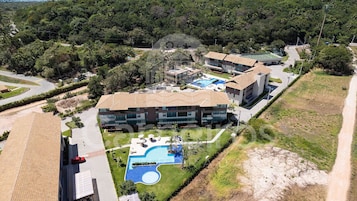 Un edificio de varios pisos con piscina, cancha de tenis y jardines ajardinados.