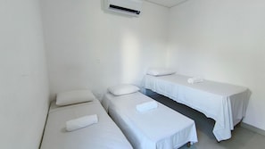 Quarto pequeno e limpo com duas camas de solteiro, cada uma com almofada e toalha enrolada.