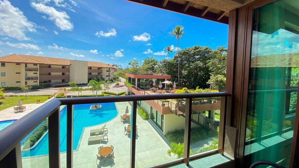 A balcony with a view of a swimming pool, outdoor seating, and a building with multiple floors. - Reserva dos Carneiros - Pé na areia (Tamandaré)