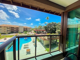 Un balcón con vista a una piscina, mobiliario exterior y un edificio de varios pisos.