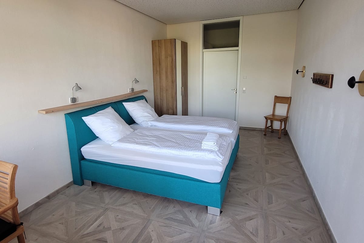 A room with a bed, a chair, a wardrobe, and a small table.