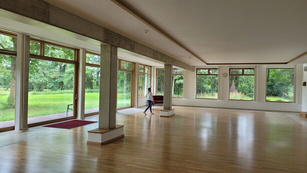 A spacious room with large windows, wooden flooring, and a red bench. - Hotel Lethehof (Wardenburg)