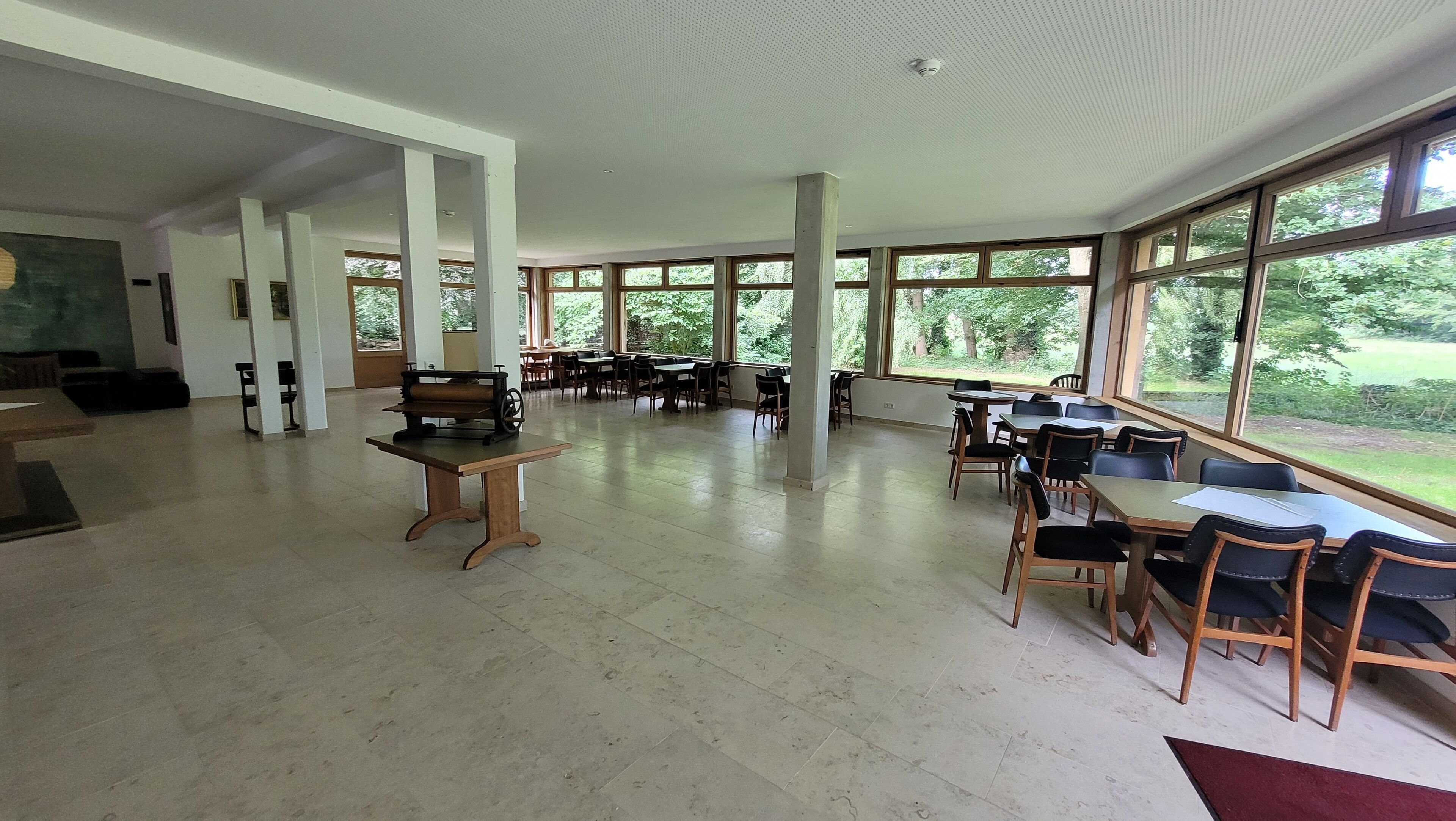 A spacious indoor area with large windows, tables, and chairs arranged for dining or meetings.