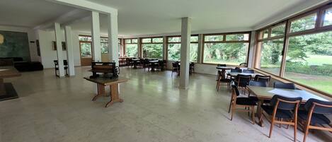 A spacious indoor area with large windows, tables, and chairs arranged for dining or meetings.