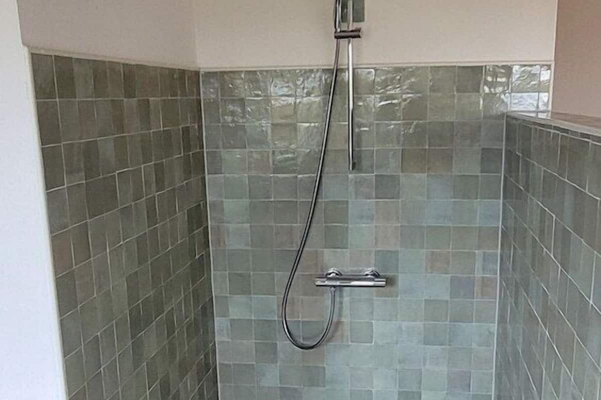 A shower with a handheld showerhead, tiled walls, and a patterned floor.