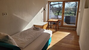 A bedroom with a bed, a small desk, and a view of the outdoors through a sliding door. - Hotel Lethehof (Wardenburg)