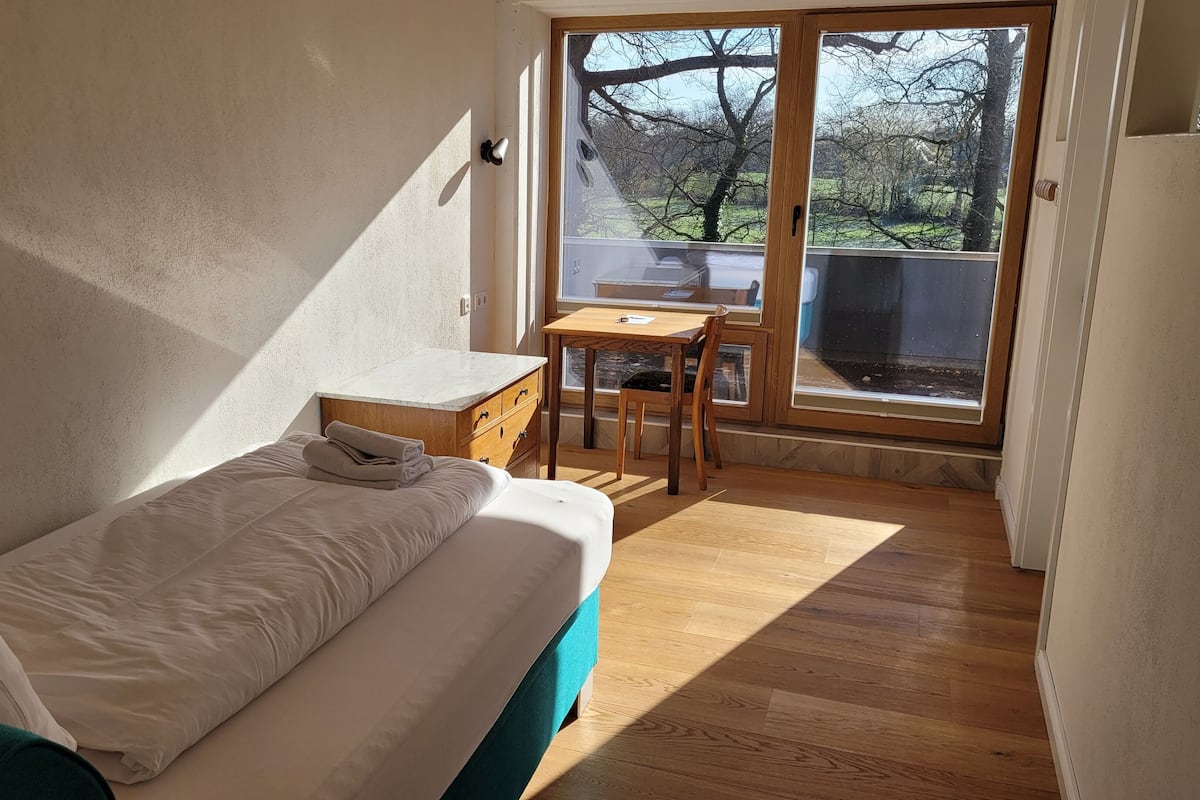 A bedroom with a bed, a small desk, and a view of the outdoors through a sliding door.