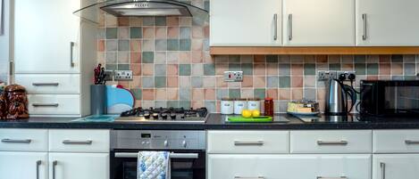 A modern kitchen with white cabinets, a gas stove, an oven, and a microwave.