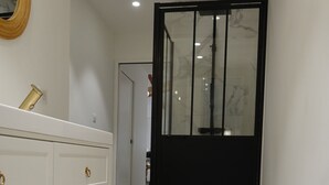 Um corredor com um aparador branco, um espelho e uma porta preta com painéis de vidro.