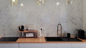 Cozinha com painel de parede em mármore, cafeteira, chaleira, torradeira e pia com torneira dourada.