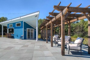 Une terrasse extérieure couverte, aménagée avec des sièges, et un bâtiment bleu en arrière-plan.