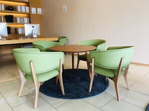 A room with a round wooden table surrounded by six green chairs with wooden legs.