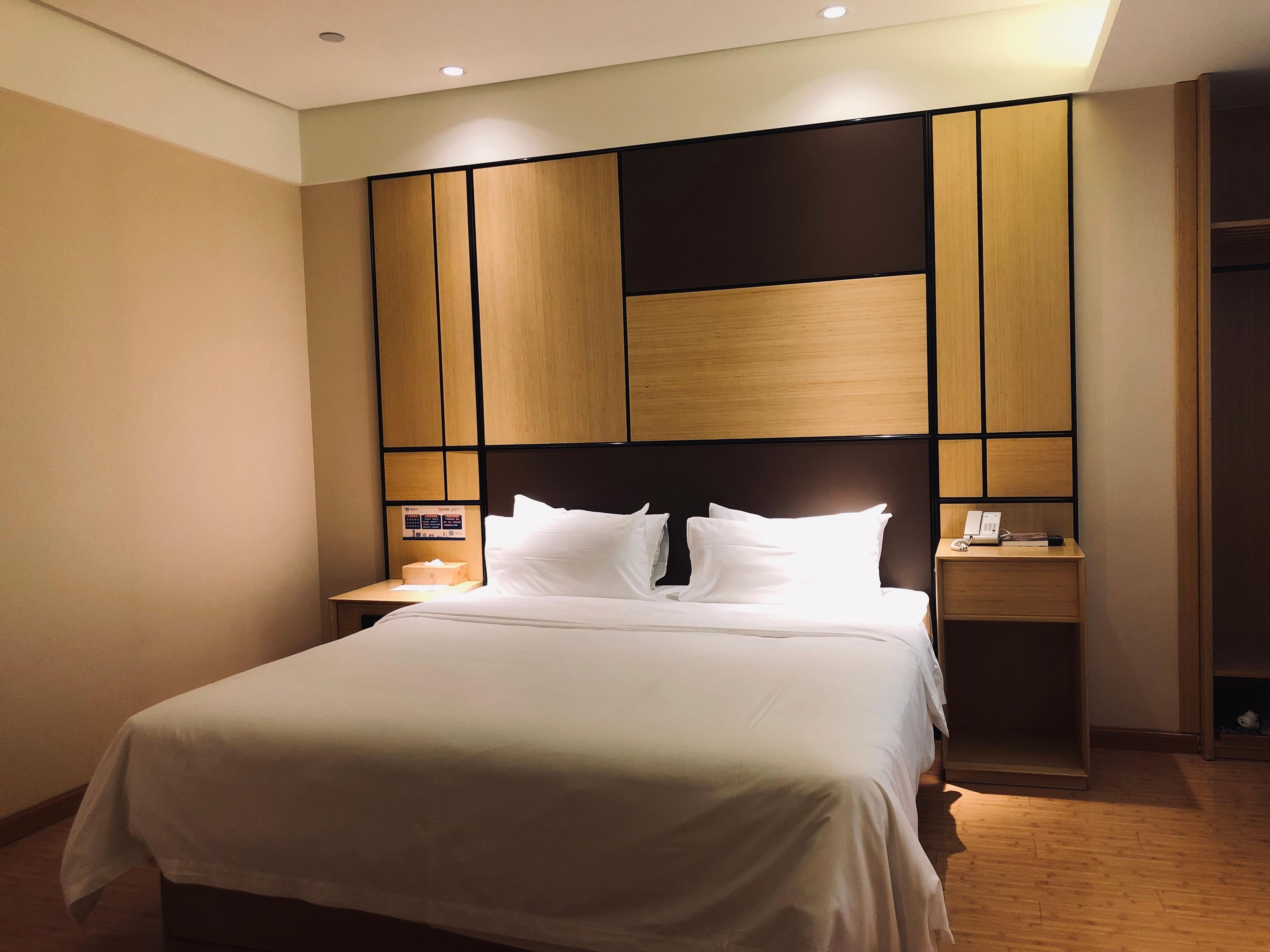 Een hotelkamer met een groot bed, houten hoofdbord, nachtkastjes en een nachtkastje met telefoon en zakdoosjes.