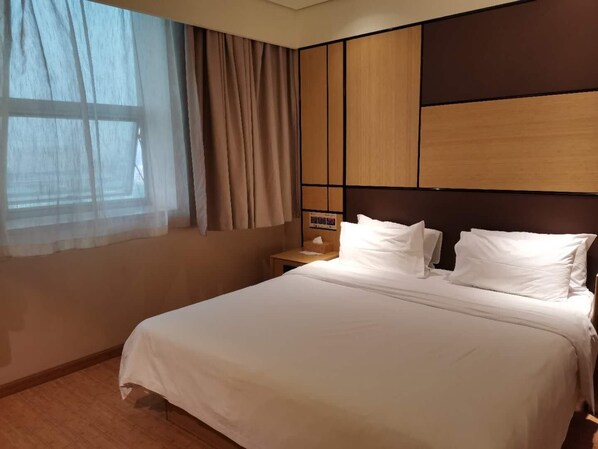 Una habitación de hotel con cama, mesita de noche, ventana con cortinas y un diseño de panel en la pared.