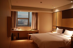 Habitación de hotel con cama, escritorio, silla, ventana con cortinas y vista a la ciudad.