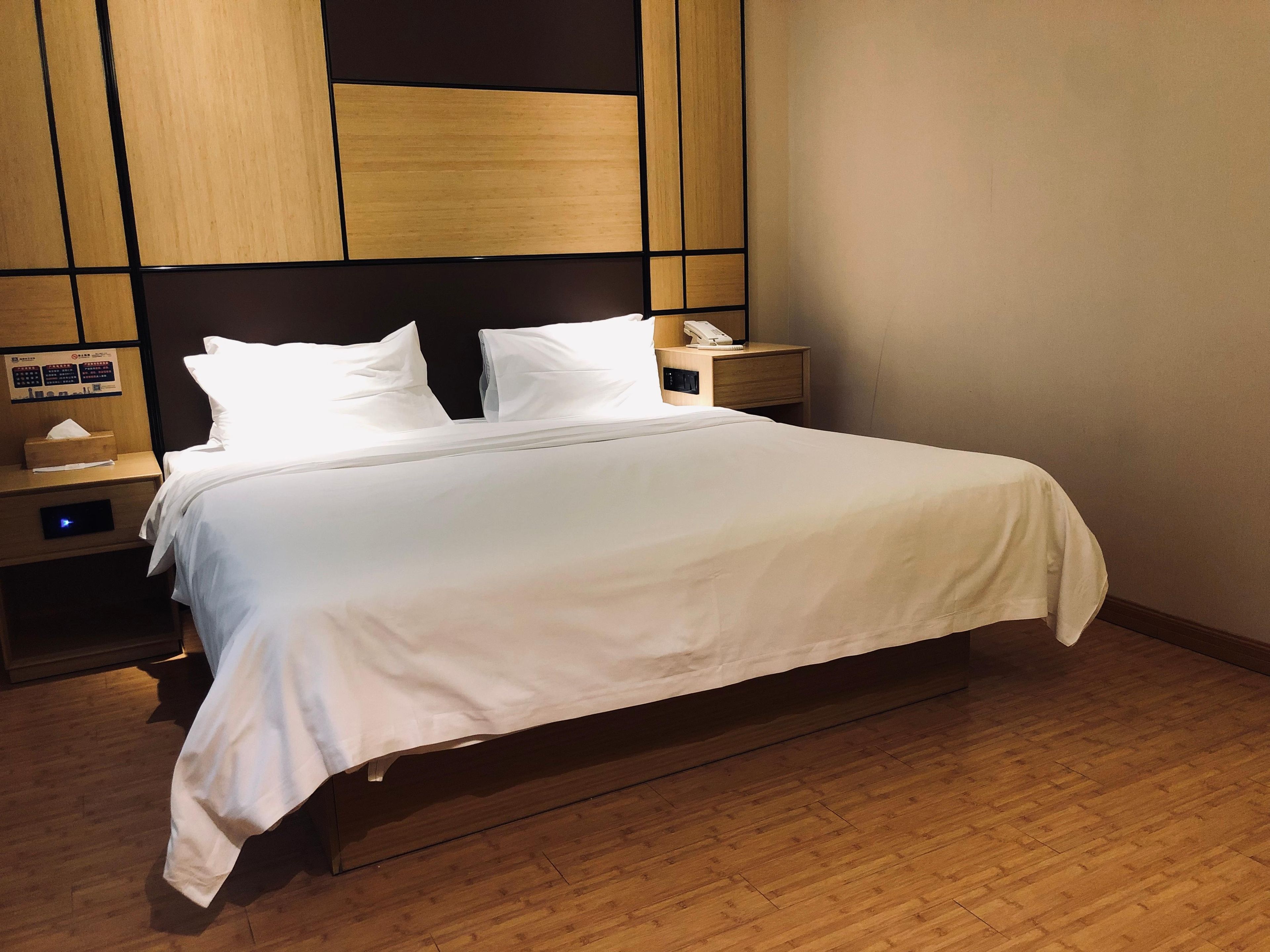 A hotel room with a bed, wooden headboard, bedside tables, and a wall-mounted control panel.