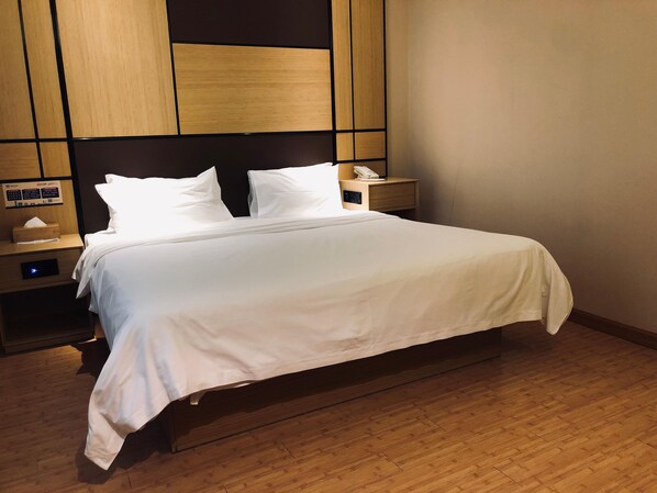 A hotel room with a bed, wooden headboard, bedside tables, and a wall-mounted control panel.