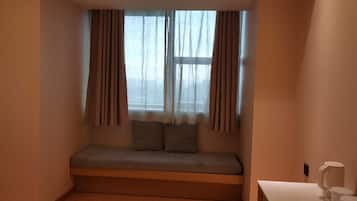 Quarto com um banco embutido, janela com cortinas, uma pequena mesa com uma caneca branca e uma tomada de parede.