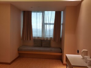 Una habitación con un banco integrado, una ventana con cortinas, una pequeña mesa con una taza blanca y un enchufe de pared.