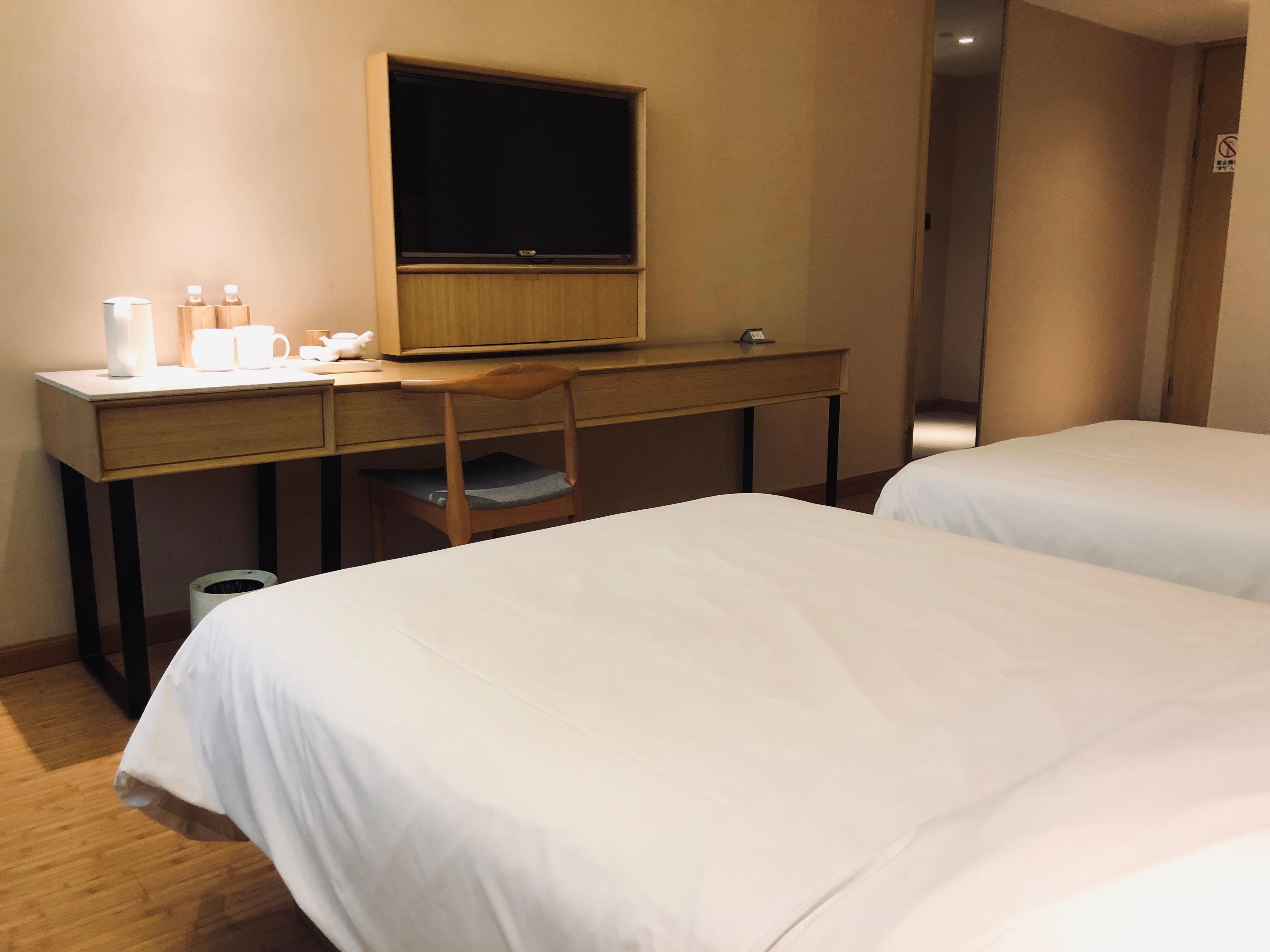 A hotel room with a desk, a television, two beds, and a trash can.