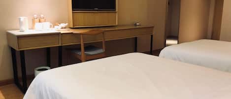 Una habitación de hotel con escritorio, televisor, dos camas y un bote de basura.