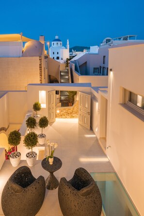 A rooftop terrace with a glass balustrade, potted plants, and a seating area. - La Madeleine Oia Suites and Caves (Santorini)