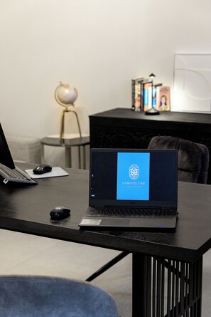 A laptop on a desk with a screen displaying "LA MADELEINE" and a desktop computer in the background. - La Madeleine Oia Suites and Caves (Santorini)