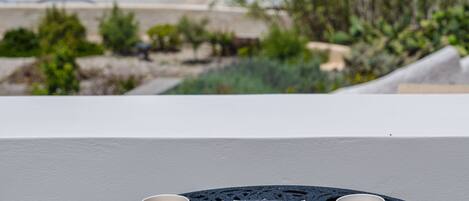 A table with two cups of coffee and a box of macarons, overlooking a coastal town with buildings and the sea.