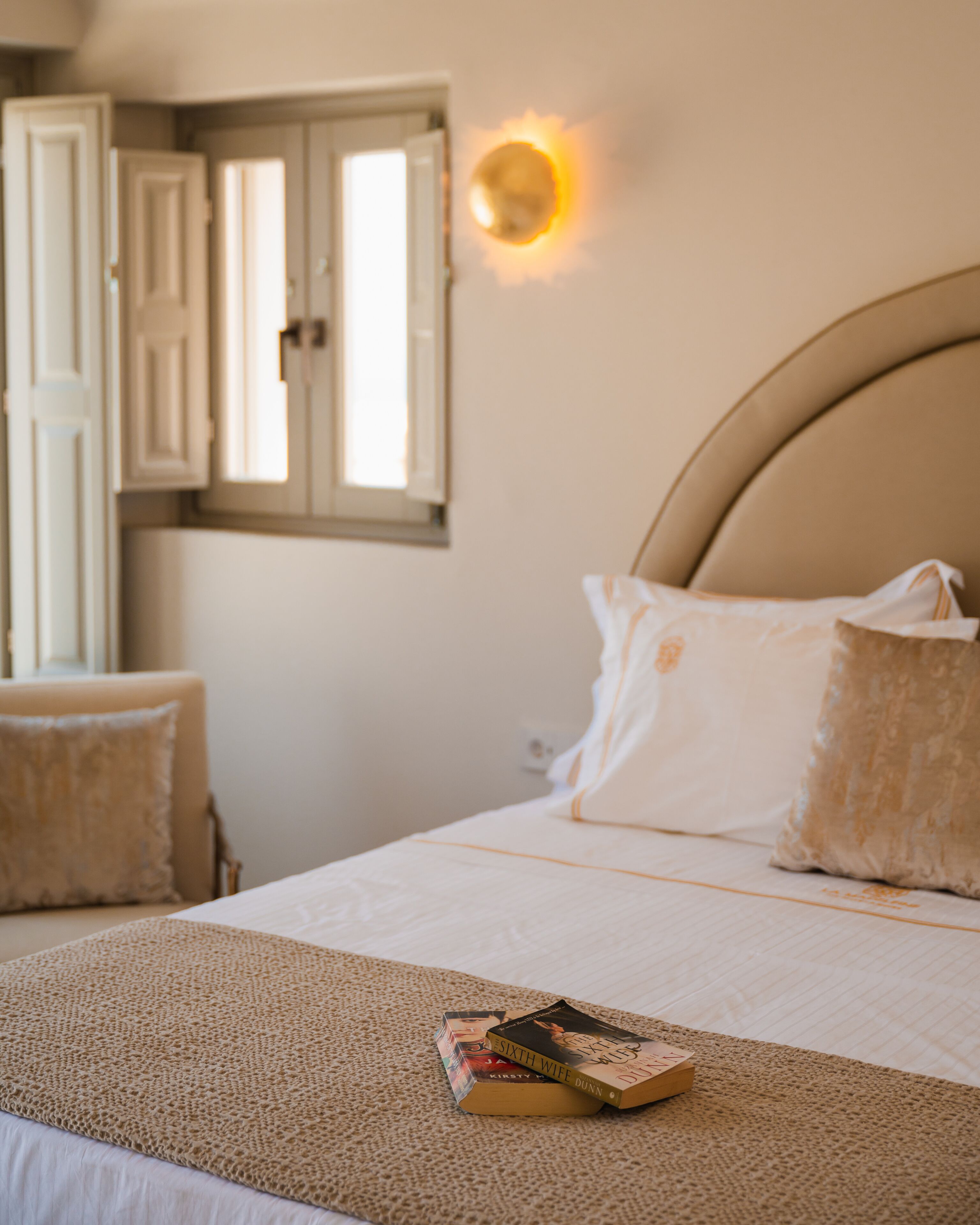 Un dormitorio con cama, almohadas, una mesita de noche y una ventana con persianas abiertas.