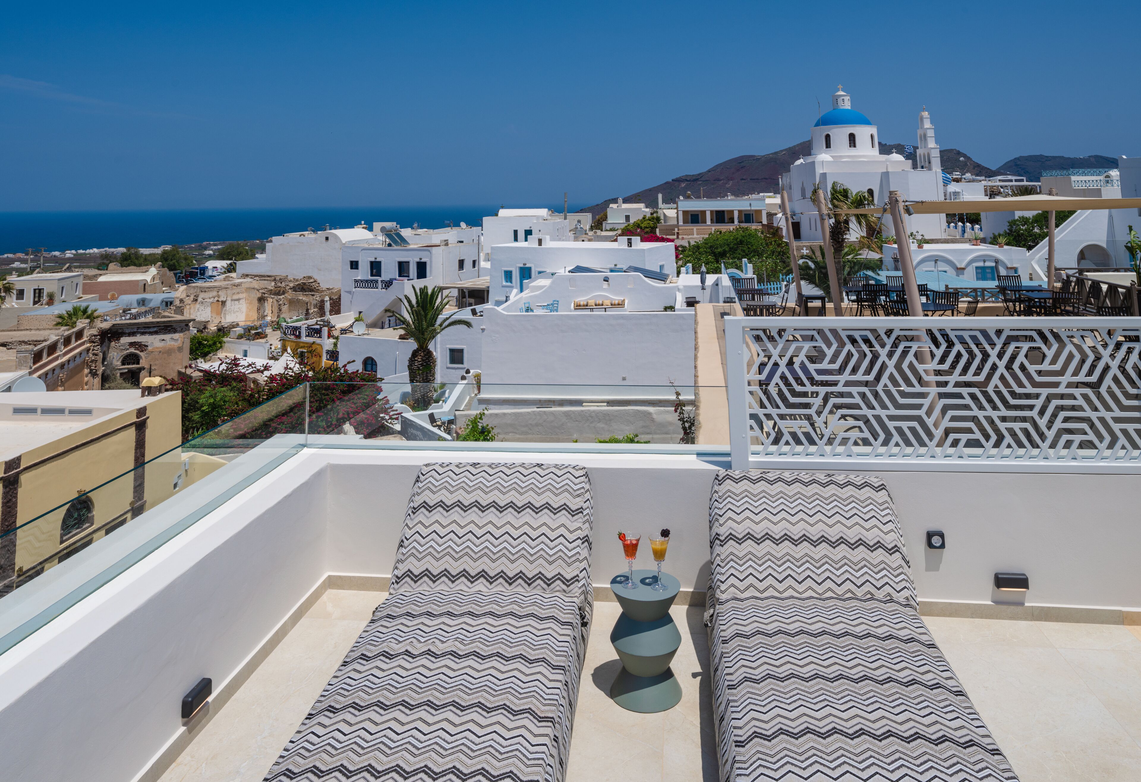 Une terrasse sur le toit avec deux chaises longues, une petite table avec des boissons et un mur décoré de motifs.
