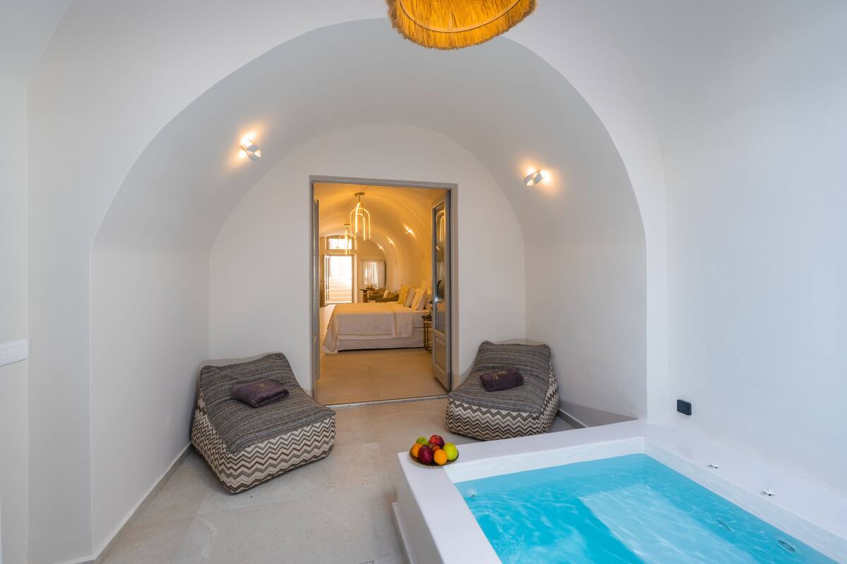 Habitación moderna con piscina, dos sillones colgantes y una cama visible a través de un arco.