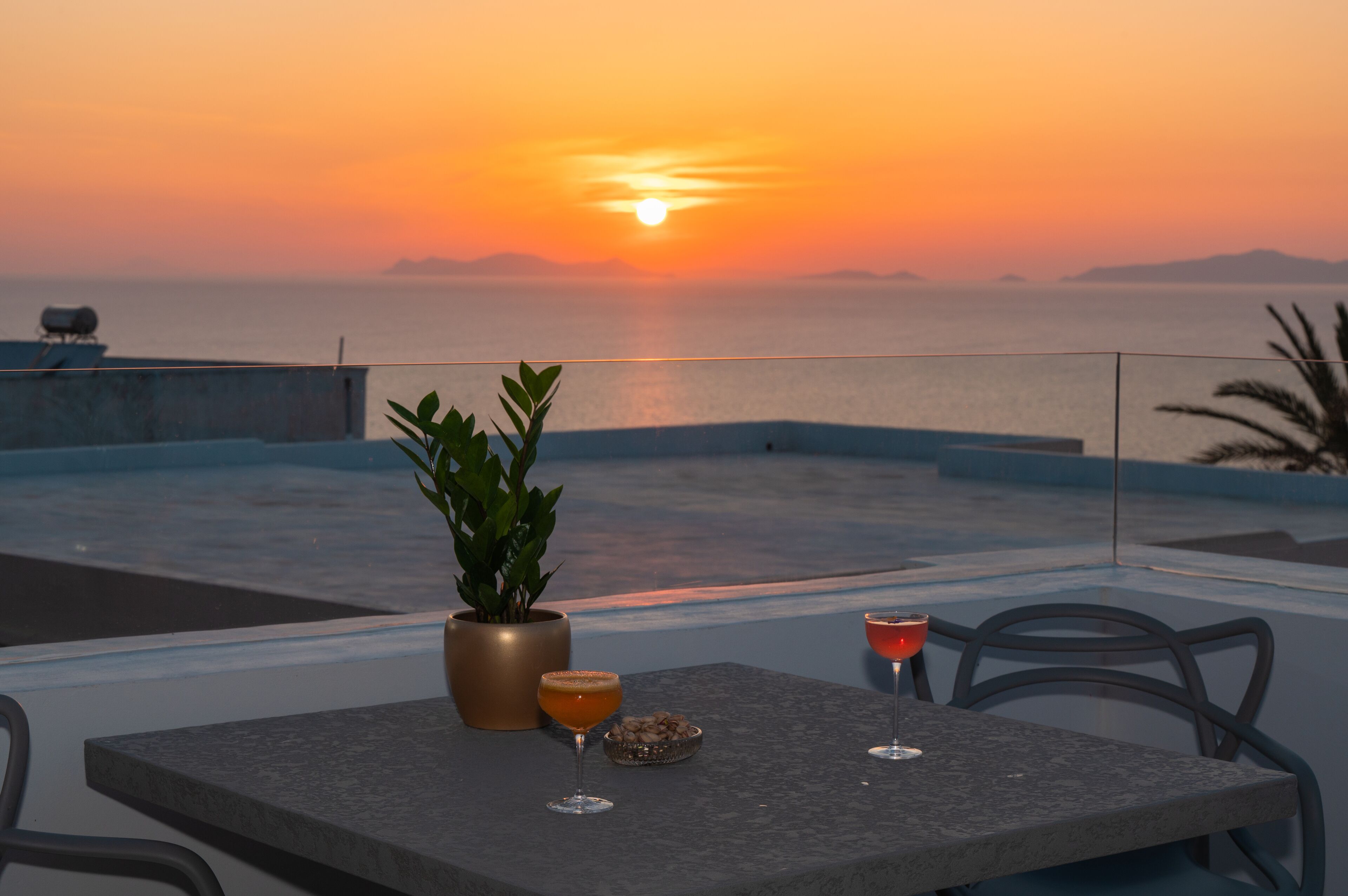 Una terraza con vista al atardecer, una mesa con bebidas y una planta en maceta.