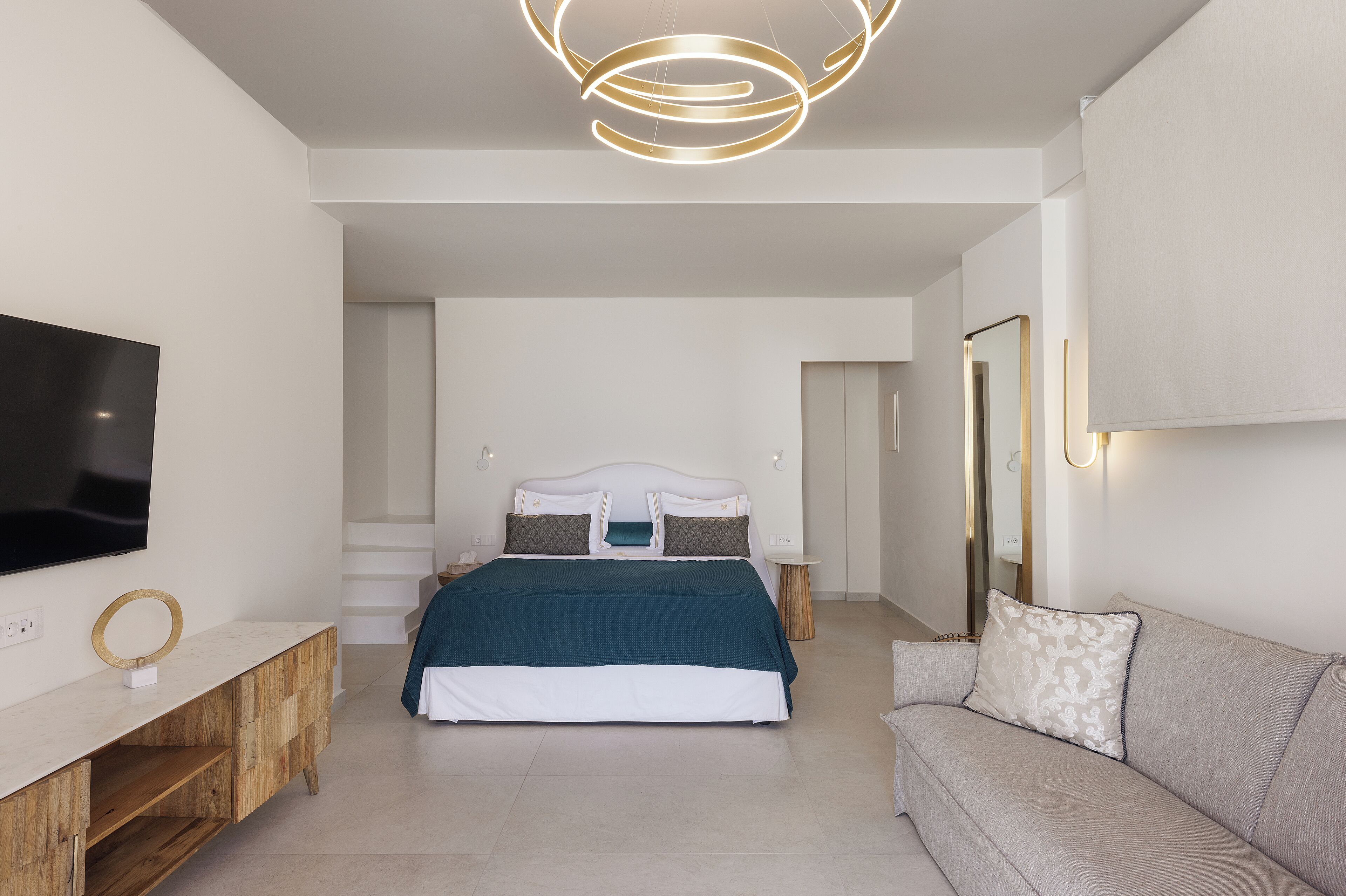A modern bedroom with a bed, a TV, a sofa, and a mirror.