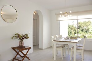 A dining area with a table and chairs, a vase with flowers, and a large window with a view of trees. - Newly renovated flat by the sea, south-facing terrace, sea 8 min. walking (Sitio de Calahonda)