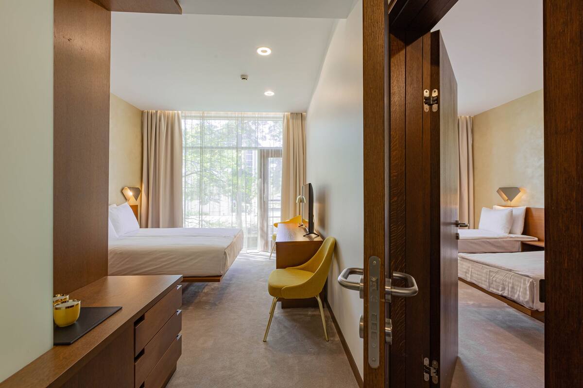 A hotel room with two beds, a desk, a chair, and a large window with curtains.