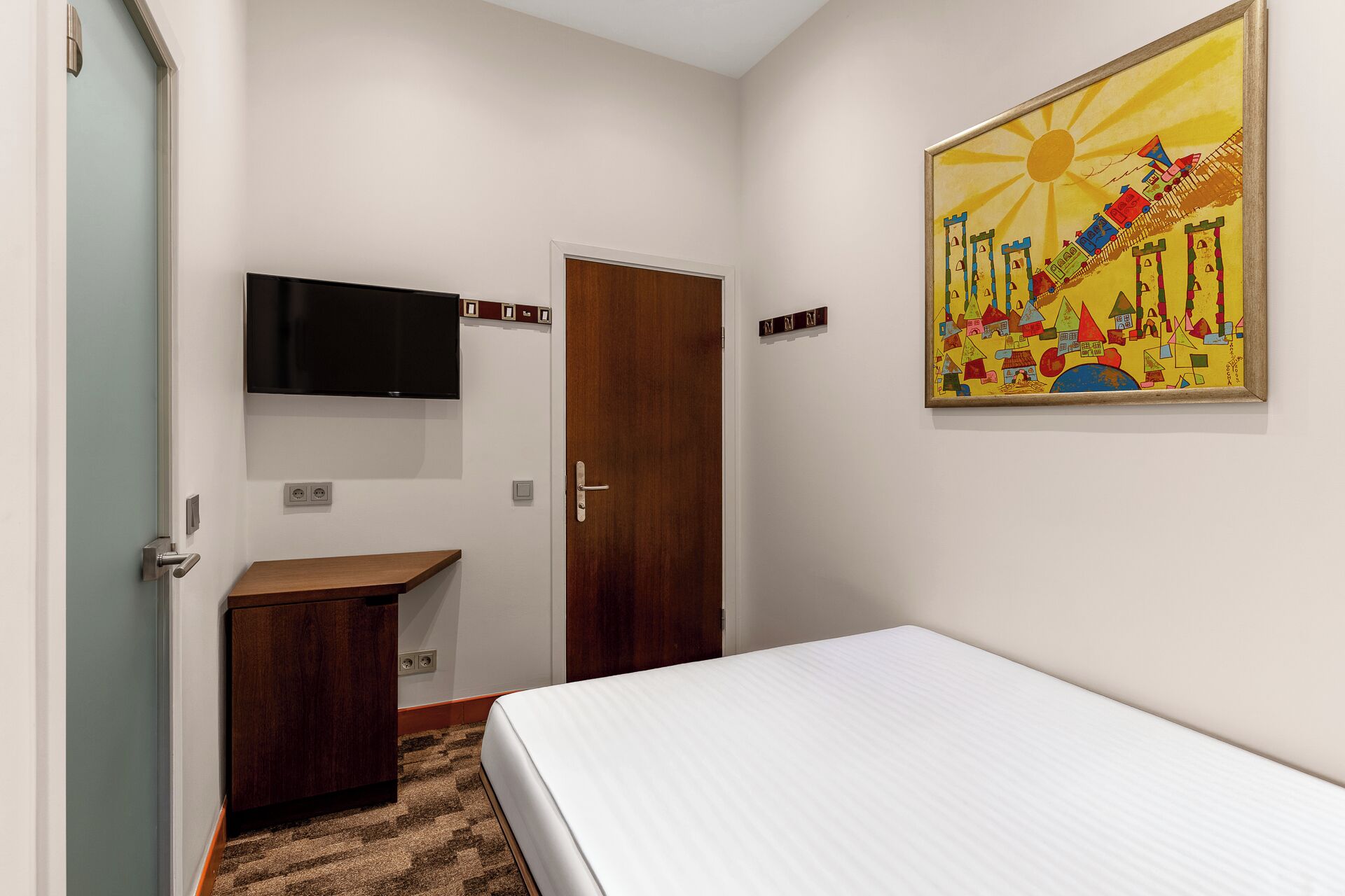 Une chambre à coucher avec un lit, un bureau, un téléviseur fixé au mur et une porte.