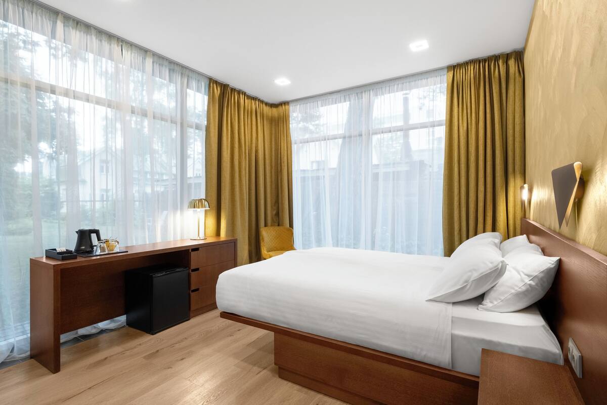 A hotel room with a bed, a desk, a lamp, and a view of the outdoors.