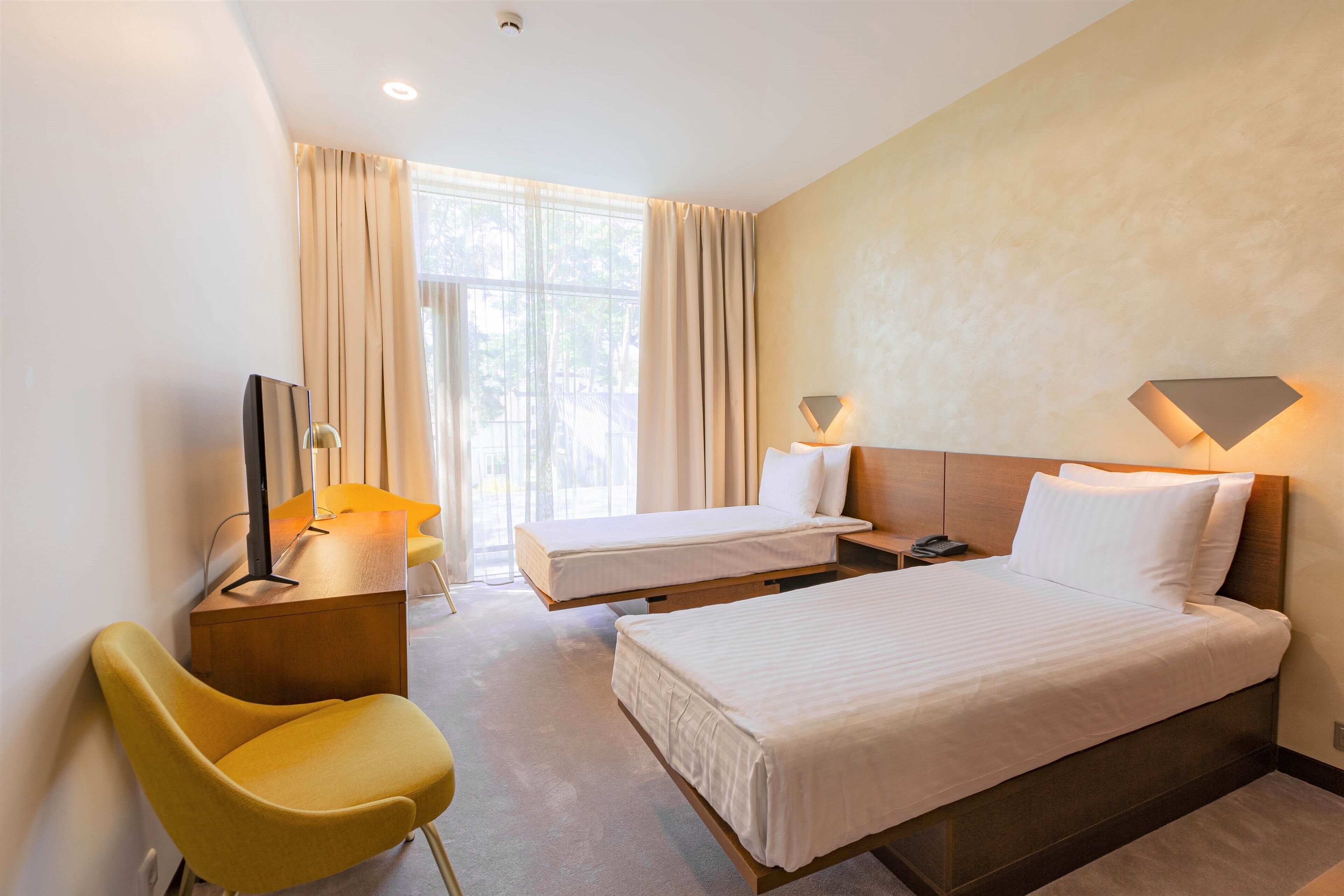 A hotel room with two beds, a desk, a chair, and a TV.