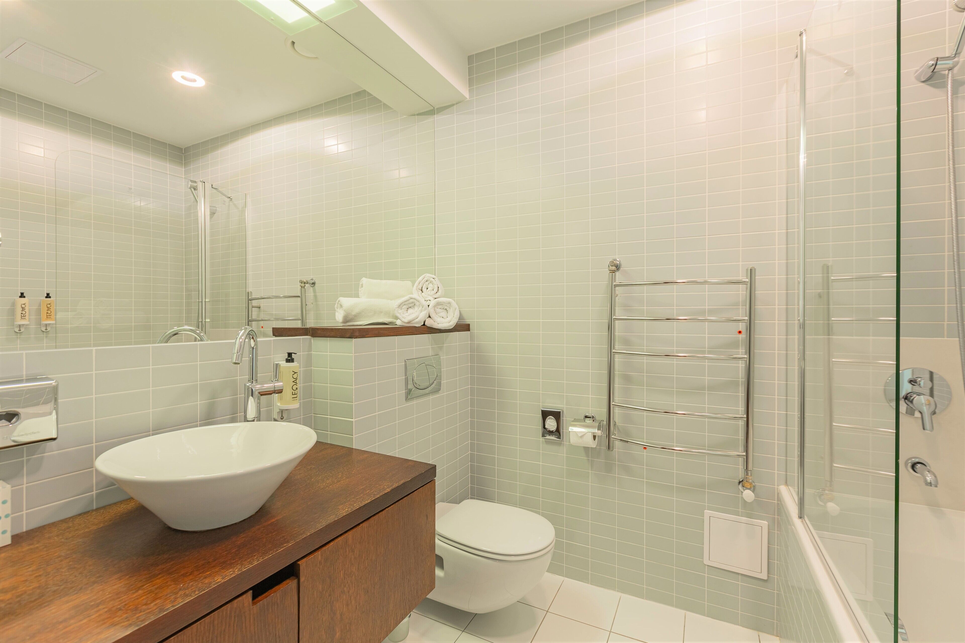 A modern bathroom with a large white sink, a toilet, and a glass-enclosed shower.