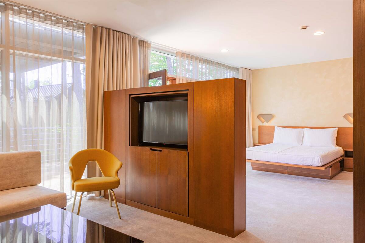 A hotel room with a bed, a TV mounted on a wooden cabinet, a sofa, and a chair.