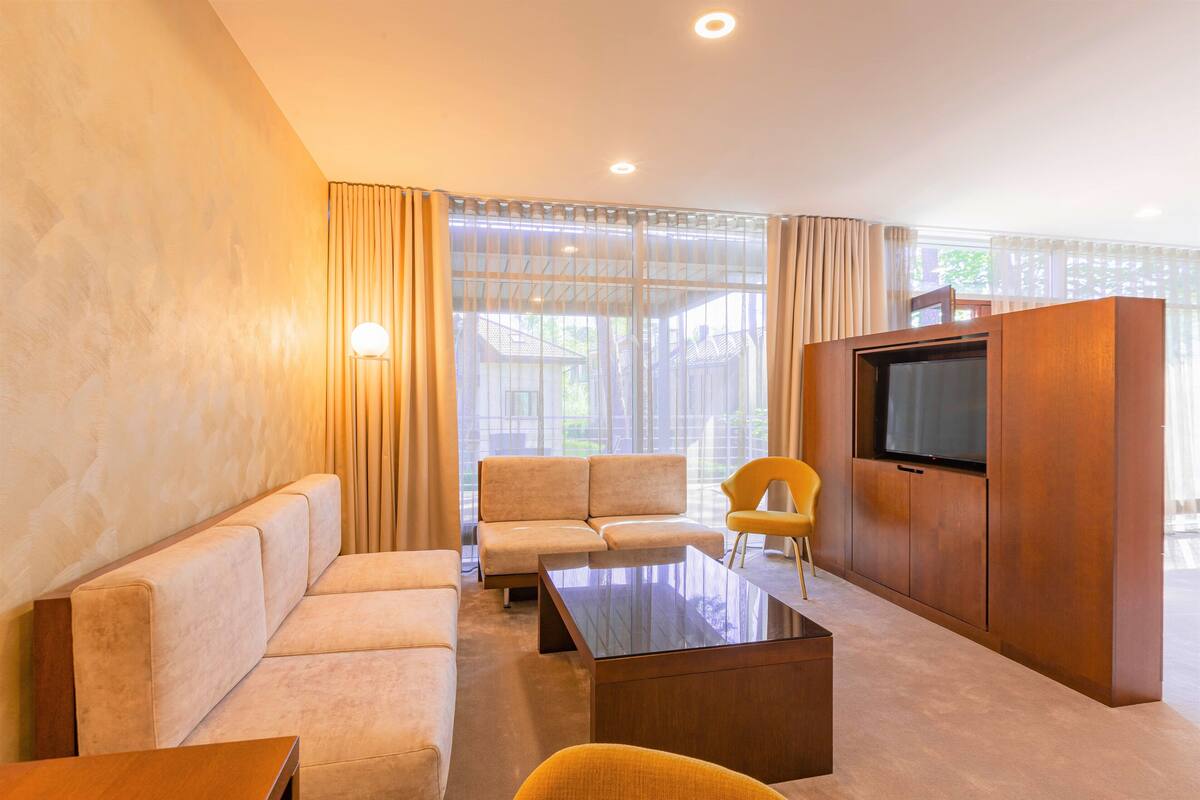 A modern living room with a sofa set, a coffee table, a TV, and a large window with curtains.