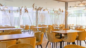 A modern dining area with yellow chairs and tables, large windows, and decorative plants. - Rixwell Collection Seaside Hotel Jurmala (Jurmala)
