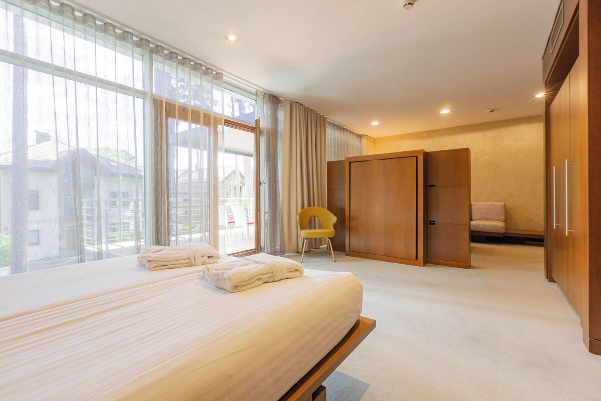 A hotel room with a large bed, a chair, a wardrobe, and a view of the outside.